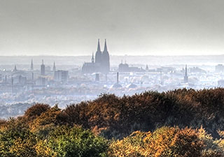 Kölner Skyline unter wolgenverhangenem Himmel vom Bergischen Land aus gesehen, im Vordergrund herbstlich-bunte Farben, Mitte der Dom. Die Stadt und der Hinmel in Grautönen