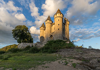 Eine Burg in Frankreich, drei dicke runde Türmemit Auskragungen und Kegeldächern, Untersicht im Abendlicht 